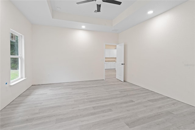 unfurnished room with light hardwood / wood-style flooring, ceiling fan, and a raised ceiling