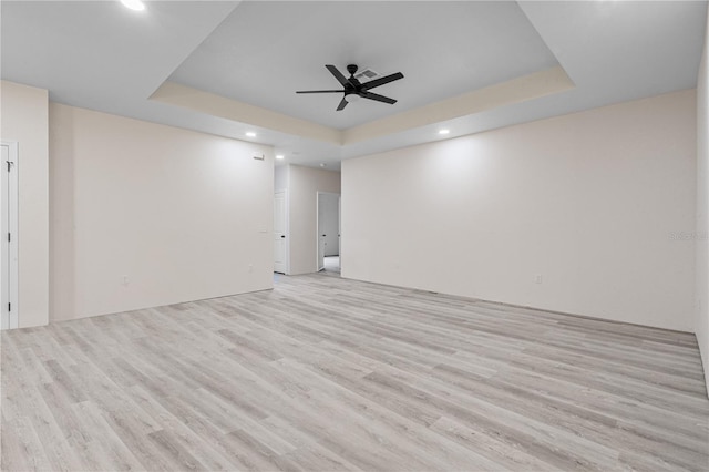 spare room with light hardwood / wood-style flooring, a tray ceiling, and ceiling fan