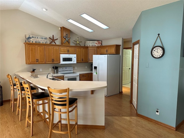 kitchen featuring a breakfast bar, white appliances, vaulted ceiling, light hardwood / wood-style floors, and kitchen peninsula