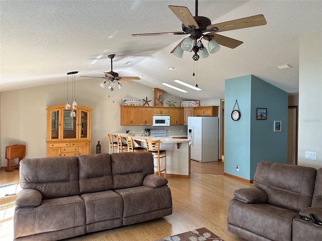 living room with a textured ceiling, light wood-type flooring, ceiling fan, and vaulted ceiling with skylight