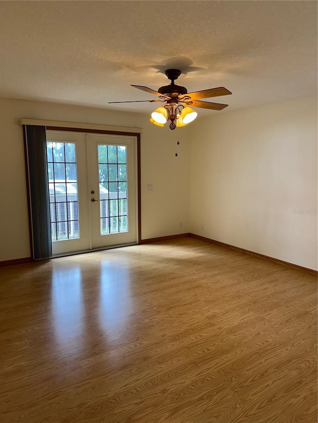 empty room with ceiling fan, light wood-type flooring, a textured ceiling, and french doors