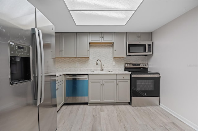 kitchen featuring backsplash, sink, gray cabinetry, light hardwood / wood-style floors, and stainless steel appliances