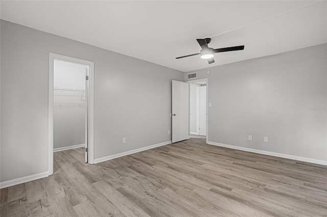 unfurnished bedroom with a spacious closet, light wood-type flooring, a closet, and ceiling fan