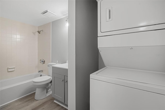 full bathroom with hardwood / wood-style floors, toilet, vanity, tiled shower / bath combo, and stacked washer / dryer