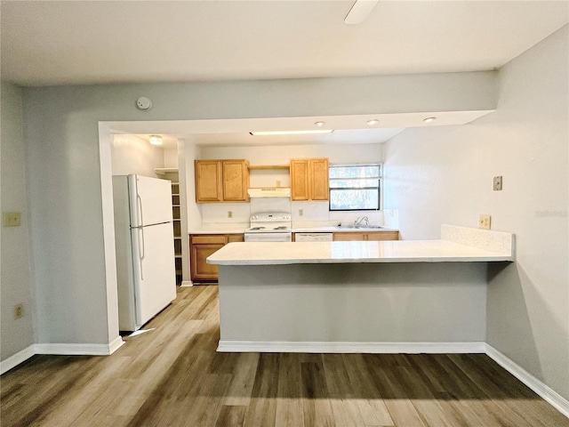 kitchen featuring white appliances, dark hardwood / wood-style floors, kitchen peninsula, and sink