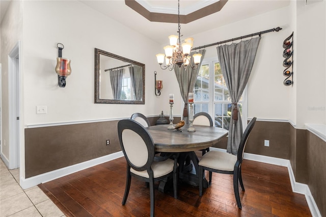 dining room with crown molding, hardwood / wood-style flooring, an inviting chandelier, and a raised ceiling