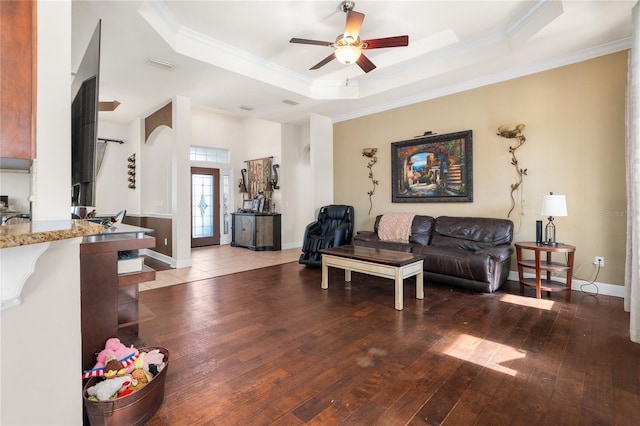 living room featuring ornamental molding, ceiling fan, dark wood-type flooring, and a raised ceiling