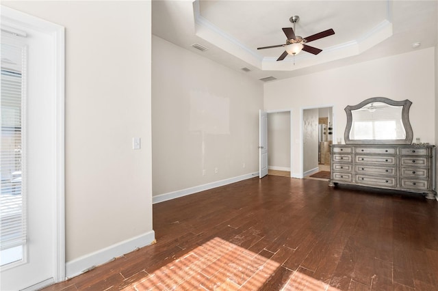 unfurnished bedroom with ceiling fan, a tray ceiling, ensuite bathroom, dark wood-type flooring, and crown molding