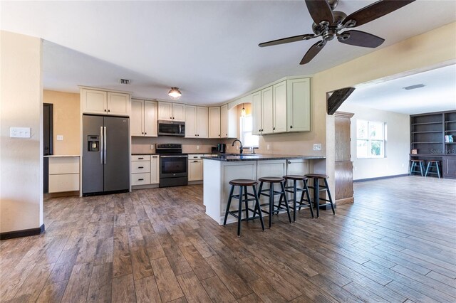 kitchen featuring kitchen peninsula, appliances with stainless steel finishes, a kitchen bar, dark hardwood / wood-style floors, and sink