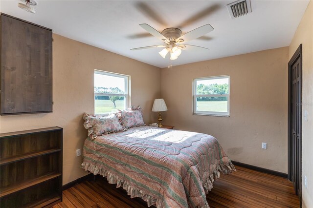 bedroom with ceiling fan, multiple windows, and dark hardwood / wood-style floors