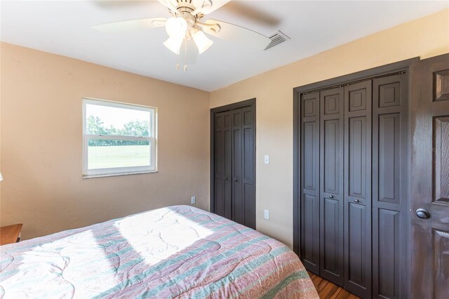 bedroom with multiple closets, hardwood / wood-style flooring, and ceiling fan