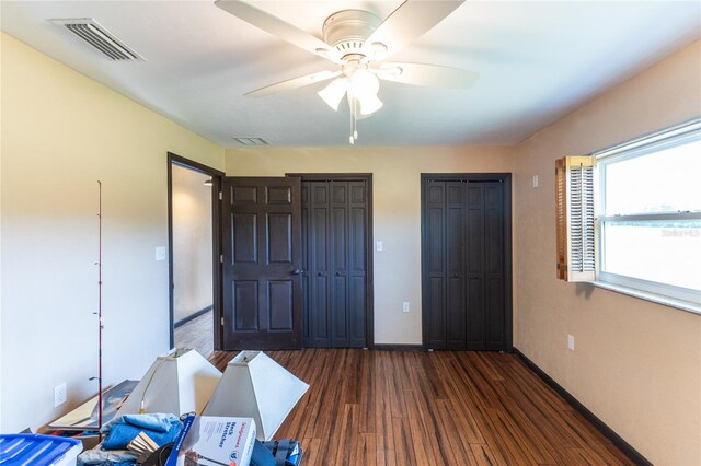 bedroom featuring dark wood-type flooring, ceiling fan, and multiple closets