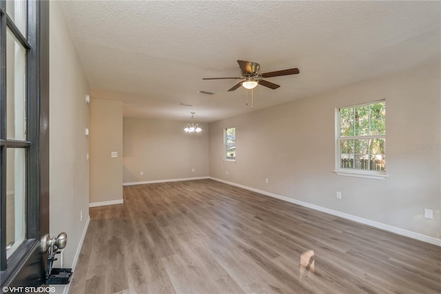 unfurnished room with hardwood / wood-style flooring, a healthy amount of sunlight, a textured ceiling, and ceiling fan with notable chandelier