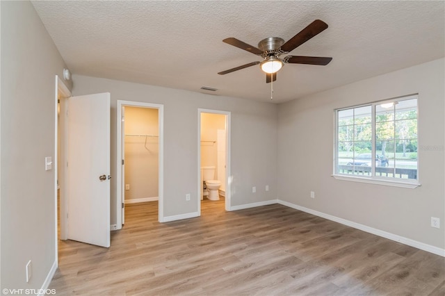 unfurnished bedroom with ensuite bathroom, a walk in closet, a closet, light hardwood / wood-style floors, and ceiling fan