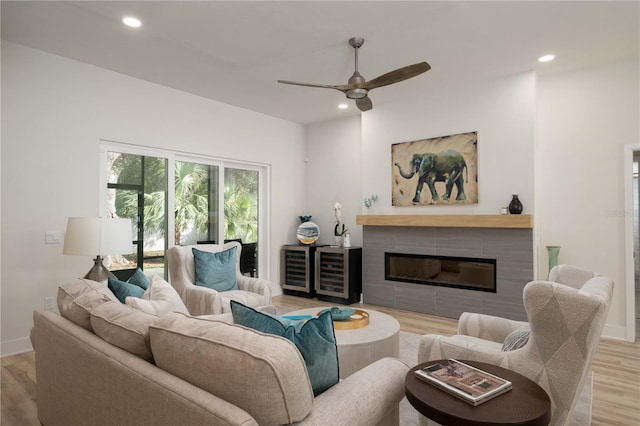 living room with a tiled fireplace, ceiling fan, and light wood-type flooring