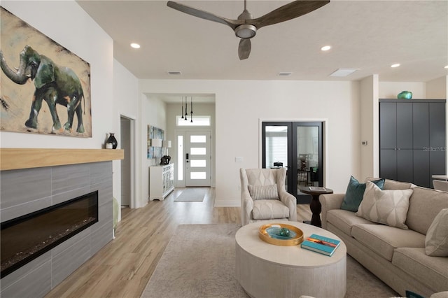 living room with a tile fireplace, ceiling fan, and light hardwood / wood-style flooring