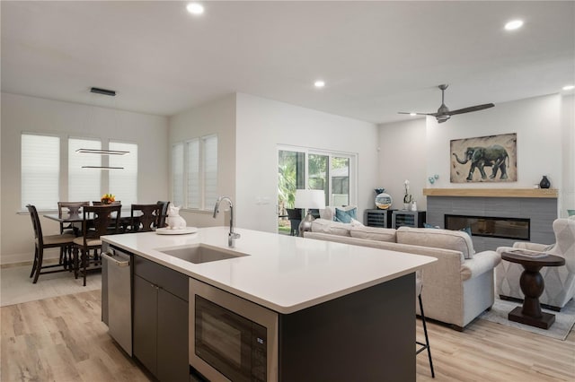 kitchen with ceiling fan, stainless steel microwave, sink, light hardwood / wood-style flooring, and a kitchen island with sink