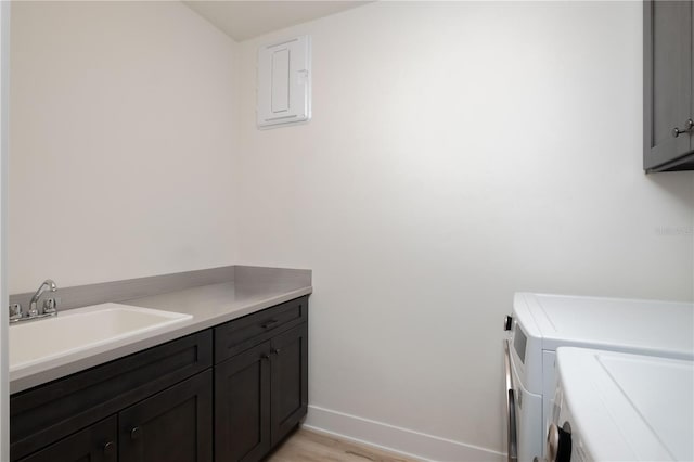 clothes washing area featuring cabinets, electric panel, sink, light hardwood / wood-style flooring, and independent washer and dryer