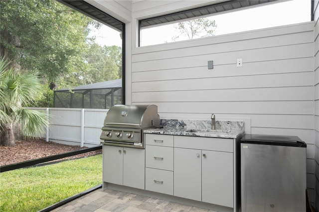 view of patio featuring glass enclosure, grilling area, and sink