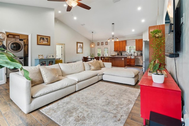 living room with high vaulted ceiling, sink, ceiling fan, hardwood / wood-style flooring, and stacked washer and clothes dryer