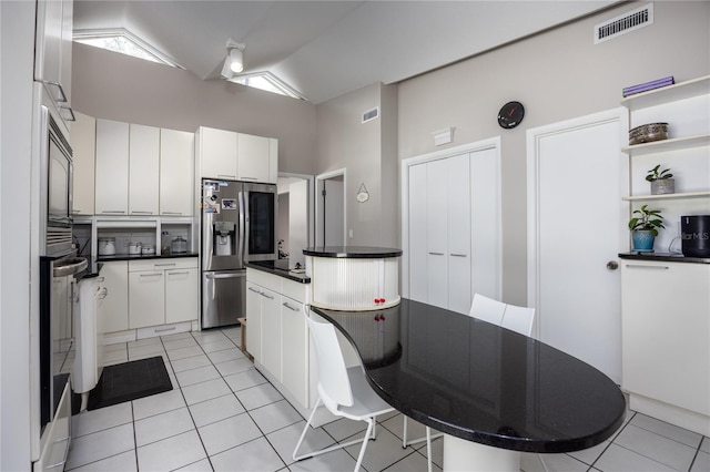 kitchen with stainless steel fridge, white cabinetry, light tile patterned floors, and lofted ceiling