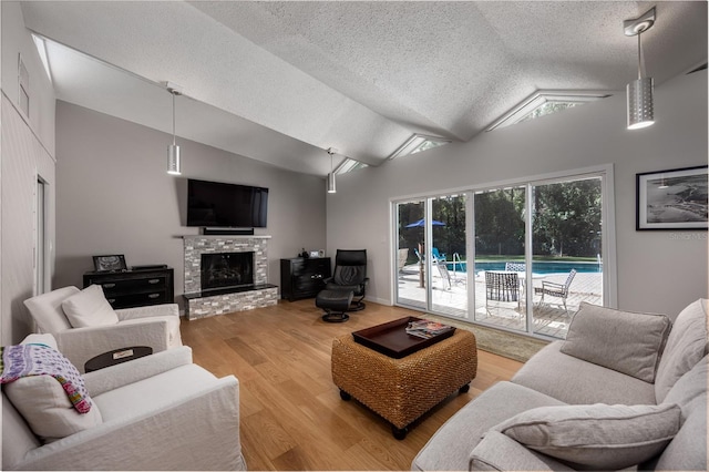 living room featuring a stone fireplace, lofted ceiling, wood-type flooring, and a textured ceiling