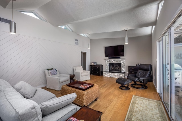 living room featuring wood walls, hardwood / wood-style flooring, a textured ceiling, a fireplace, and vaulted ceiling