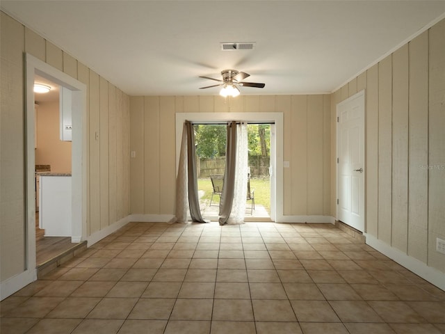 empty room featuring wood walls, crown molding, light tile patterned floors, and ceiling fan