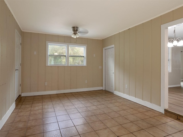 tiled spare room with crown molding, ceiling fan with notable chandelier, and wooden walls