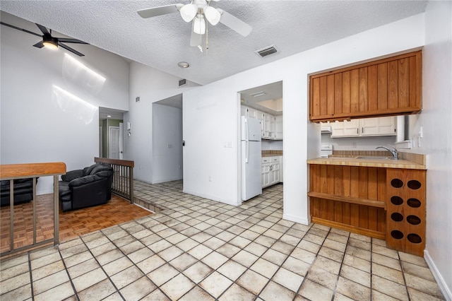 kitchen with visible vents, a textured ceiling, open floor plan, freestanding refrigerator, and light countertops