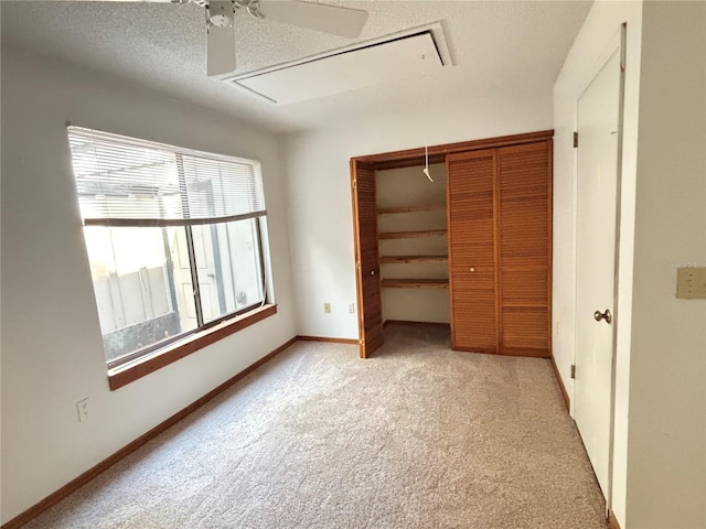 unfurnished bedroom with baseboards, attic access, a closet, a textured ceiling, and carpet flooring