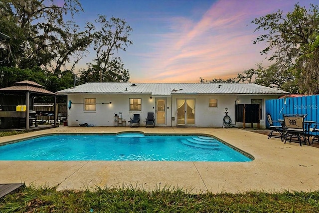 pool at dusk with a patio area and a gazebo