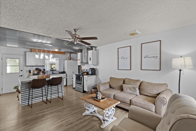 living room with ceiling fan, sink, a textured ceiling, and hardwood / wood-style flooring