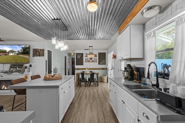 kitchen featuring decorative light fixtures, a kitchen island, a kitchen bar, sink, and white cabinets