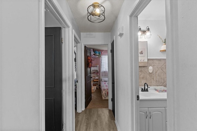 hall featuring a textured ceiling, tile walls, light hardwood / wood-style flooring, and sink