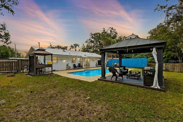 pool at dusk featuring a gazebo, a yard, and a fire pit