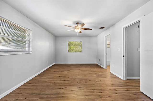 empty room with plenty of natural light, ceiling fan, and dark hardwood / wood-style flooring