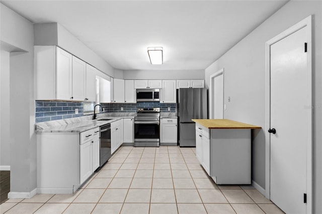 kitchen featuring backsplash, appliances with stainless steel finishes, light tile patterned floors, sink, and white cabinets