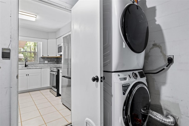 laundry room featuring light tile patterned flooring, stacked washer / dryer, and sink