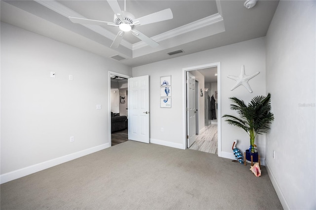 unfurnished bedroom with crown molding, ceiling fan, light colored carpet, and a raised ceiling