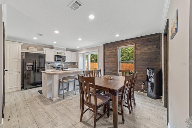 dining area with a textured ceiling, heating unit, crown molding, and wooden walls