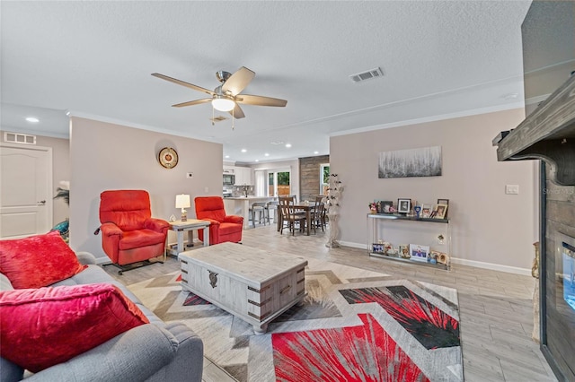 living room featuring ceiling fan, crown molding, a textured ceiling, and light wood-type flooring