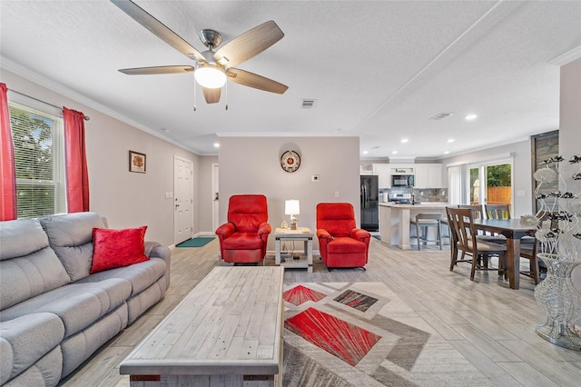 living room featuring light hardwood / wood-style flooring, ornamental molding, ceiling fan, and a textured ceiling