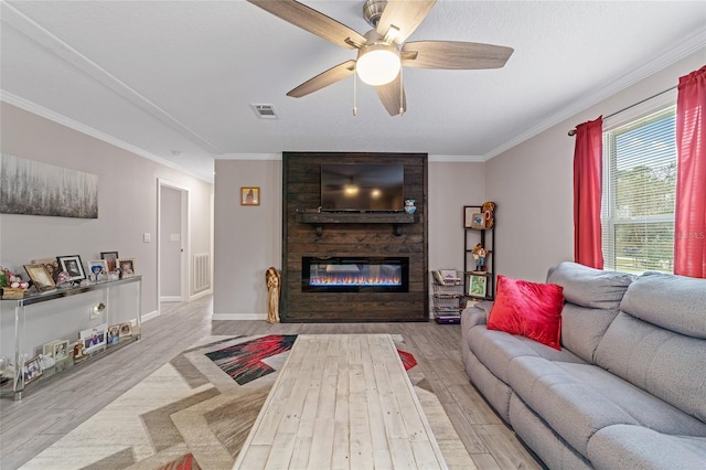 living room with light hardwood / wood-style flooring, ornamental molding, ceiling fan, and a large fireplace