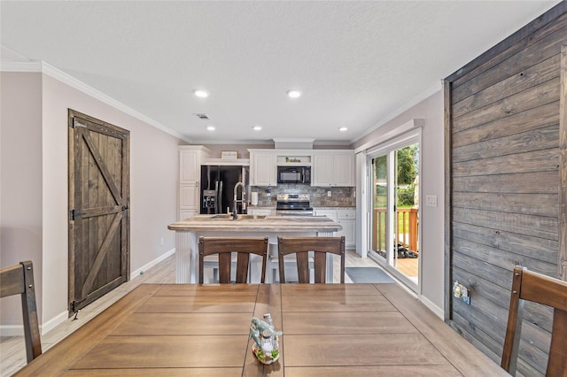 dining space with ornamental molding, light wood-type flooring, a barn door, and a textured ceiling