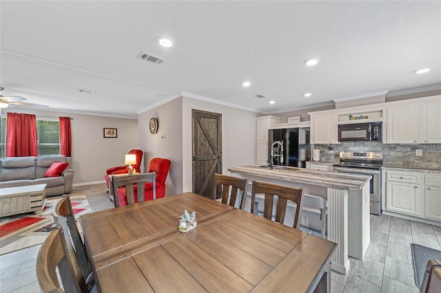 dining space featuring light wood-type flooring, a barn door, ceiling fan, and ornamental molding