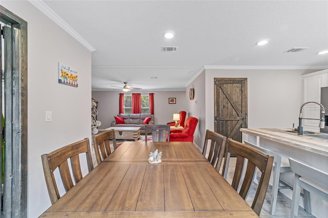 dining space featuring a barn door, ceiling fan, ornamental molding, and sink