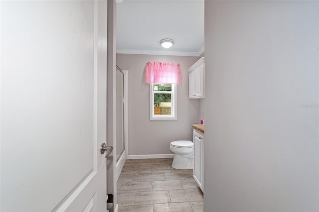 bathroom with vanity, toilet, a shower with shower door, and crown molding