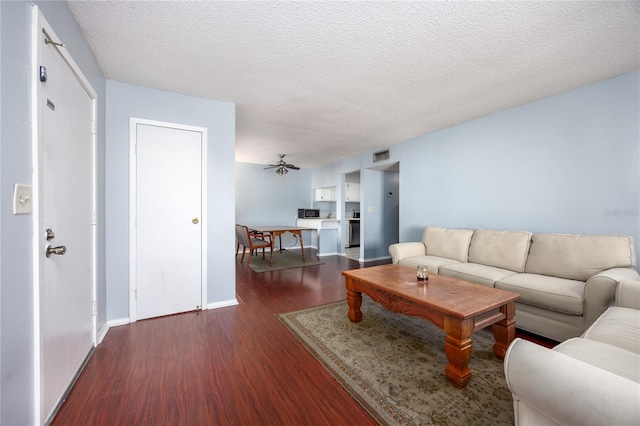 living room with a textured ceiling, dark wood-type flooring, and ceiling fan