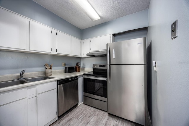 kitchen featuring sink, light wood-type flooring, white cabinetry, appliances with stainless steel finishes, and a textured ceiling